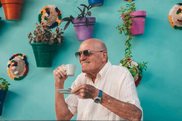 Portrait of smiling relaxed senior man sitting at cafe table in a flowered patio with colored vases...
