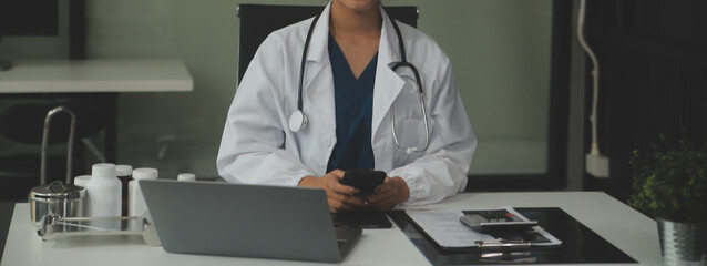 Serious female doctor using laptop and writing notes in medical journal sitting at desk. Young...