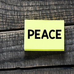 PEACE word on a small sheet of paper and a wooden background.