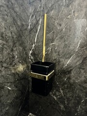 A black and gold toilet brush holder is mounted on a wall