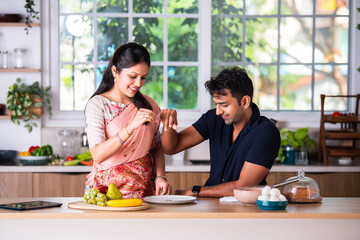 Asian indian married young couple sprinkling something on empty plate in the kitchen