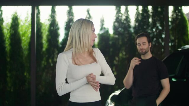 The boyfriend and the girlfriend had a dispute. The girl is deeply offended by her young man's behavior. She screams and scolds him in the street. A young man with a headache leaned on his car to rest
