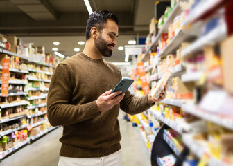 Man using smartphone to compare products in supermarket