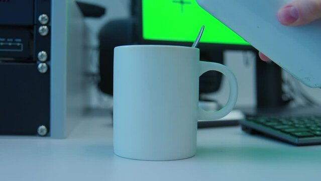 Adding a hot water to a white coffee cup sits on a desk next to a computer monitor. The scene is set in a workspace, with a keyboard and mouse nearby. Concept of productivity and focus