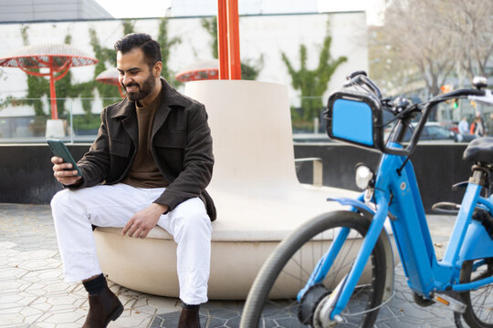 Casual urban man using smartphone near bike-sharing station