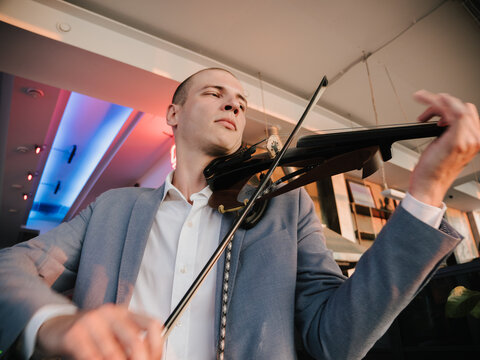 Violinist engages with electric violin, passion in his expression, in vibrant venue lighting.