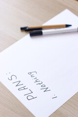A white blank note or sheet of paper is on a wooden table background. To do list concept with no plans