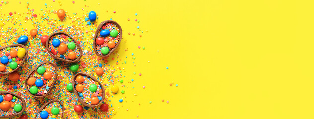 Chocolate eggs with candies and sugar colored sprinkles on a yellow background, top view. Easter...