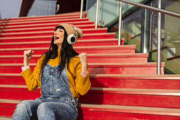 Joyful Young Woman with Headphones on Vibrant Red Steps