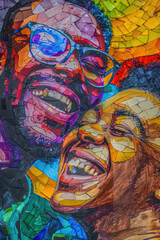 A painting featuring two men with glasses on, looking at the viewer with happy expression