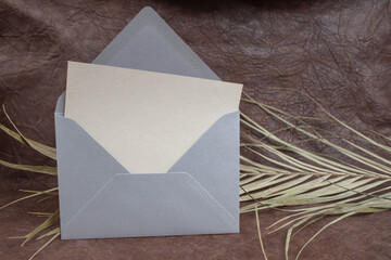 Gray blank postcard with a silver envelope,  and a dried palm leaf on genuine leather background,...