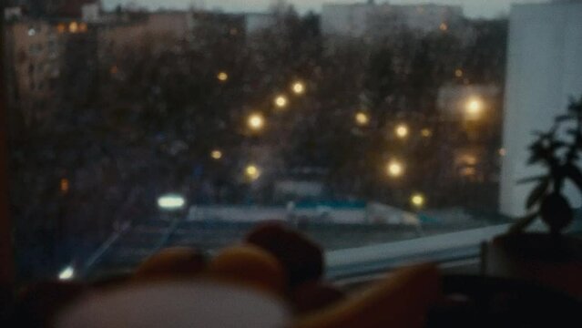 City being seen by someone in a window, the camera refocus on the drops of rain in the window and the bowl of fruit