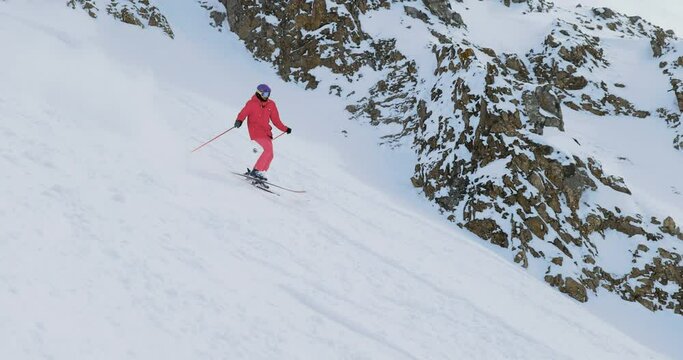 Female Freeride skier skiing descending a steep mountain making turns spraying powder snow