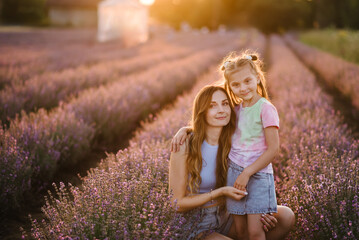 Mother embraces little daughter in lavender field enjoying scent on summer day at sunset. Mom hugs...