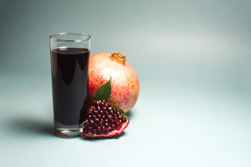 Pomegranate juice in a transparent glass in close-up and fresh pomegranate on a light background.