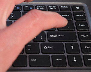 hand about to touch enter key, selective focus of enter key on notebook keyboard