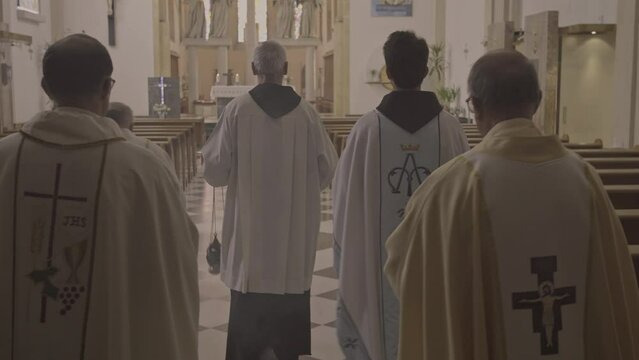 Christian priests walking in white robes during liturgy ceremony back view tracking shot. Prayers carrying censer in church. Ministers procession concept