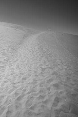 Grayscale view of a sandy desert dune covered in footprints.