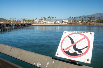 sign no diving and no jumping at the pier with palm trees and sandy beach in Santa Barbara, USA