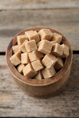 Brown sugar cubes in bowl on wooden table, closeup