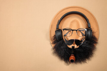 Man's face made of artificial mustache, beard, glasses and hat on beige background, top view. Space...