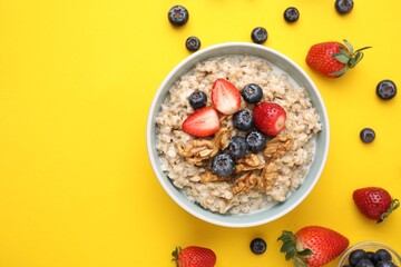 Tasty oatmeal with strawberries, blueberries and walnuts in bowl surrounded by ingredients on...