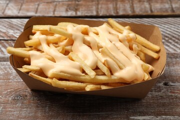 Delicious French fries with cheese sauce on wooden rustic table, closeup