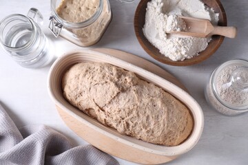 Fresh sourdough in proofing basket, flour and water on light table, flat lay