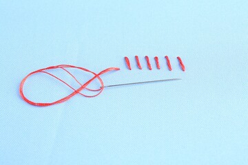 Sewing needle with thread and stitches on light blue cloth, above view