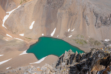Dizzying view from above to green alpine lake among sharp rocks and sheer crags in sunlight. Dizzy...