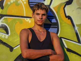 A guy in a black T-shirt stands against the background of graffiti