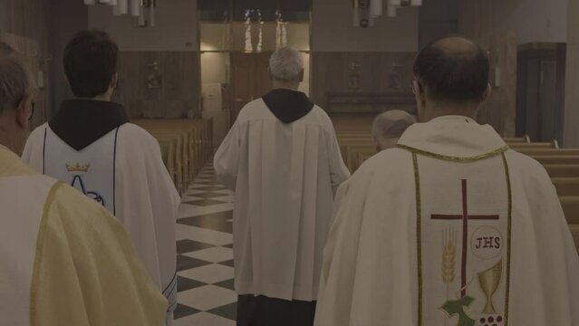 Procession of Ministers walking through church aisle after liturgy back view tracking shot. Priests in white robes ending christian religious ceremony in cathedral