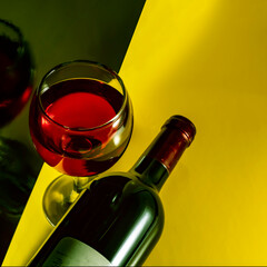 Glass and bottle of red wine on a yellow background. Square image.