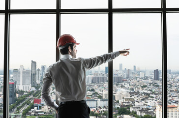 Back view engineer man standing and looking out of high rise office windows
