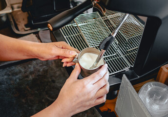 Close-up of Barista hand using high-pressure steam-operated milk frother to prepare a cappuccino and latte coffee milk