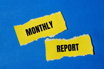 Monthly report words written on ripped yellow paper pieces with blue background. Conceptual monthly...