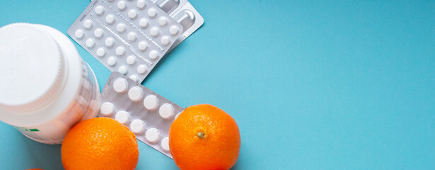 Orange fruits vs pills and medicine top view. Vitamin C close up on blue background with copy...