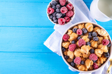 Tiny breakfast croissants cereals with fresh berries and milk. Bowl portions with trendy fresh baked mini petite croissants with raspberry and blueberry, dessert morning snack