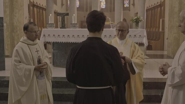 Monk ordination ceremony in christian church zoom out dolly shot. Ordinand and priests standing near sanctuary during religious ceremony. Consecration concept