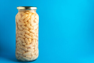 A clear jar filled with cooked white beans sits against a vibrant blue background. The beans are neatly packed, showcasing their smooth texture and light color