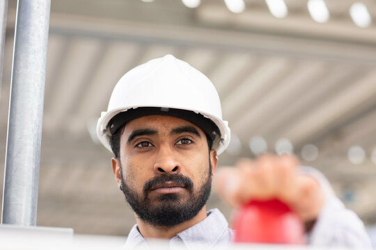 A focused man wearing a white hard hat is looking intently at something, pressing the red button