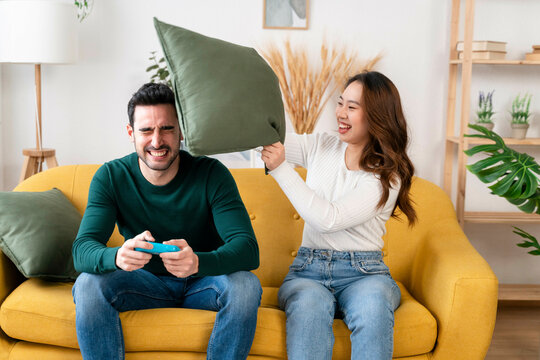 Woman hitting man with pillow as he plays video game