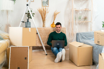 Man with laptop sitting on floor among moving boxes.
