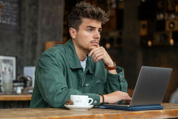 Man pondering at laptop in a cafe.