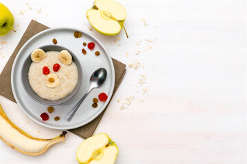 Funny cute kids childrens baby's healthy breakfast lunch oatmeal porridge in bowl look like bear face decorated with apple,banana,dried berry fruits. dessert food art on white wooden table.copy space