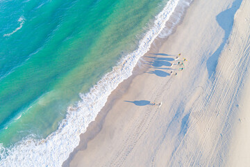 a group of surfers walking with their surfboards under their arms along the shore of a beach,...