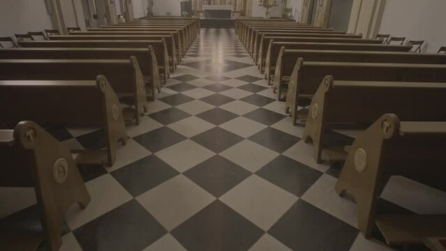 Moving forward through aisle to sanctuary in empty church. Christian cathedral interior with wooden pews rows, altar and black and white tile floor tilt up shot
