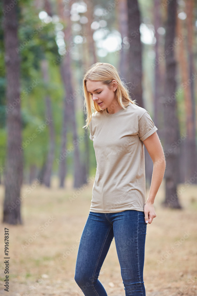 Wall mural Attractive blue eyed blonde woman walk on the city park. Girl wear beige t-shirt, pink bag and look happy and smiles.