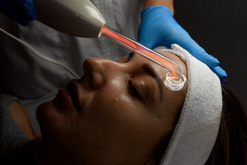 Cosmetologist in a blue gloves makes a massage with a microcurrent apparatus on a face