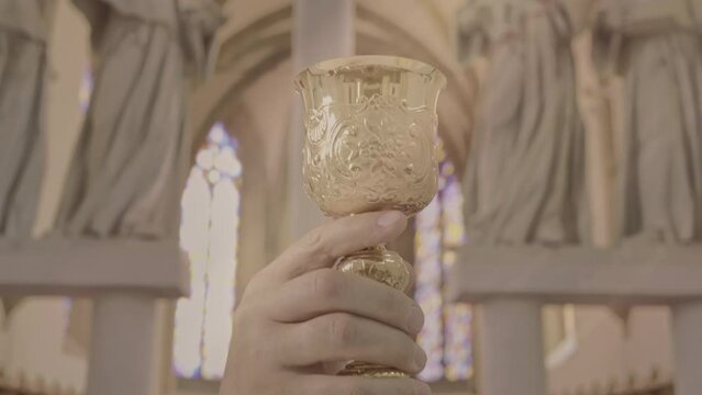 Christian priest lifting altar wine while celebrating Eucharist close up handheld shot. Catholic clergyman holding golden chalice during Holy Communion ritual in church